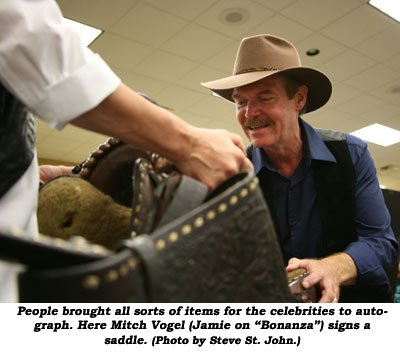 People brought all sorts of items for the celebrities to autograph. Here Mitch Vogel (Jamie on "Bonanza") signs a saddle.  (Photo by Steve St. John.)