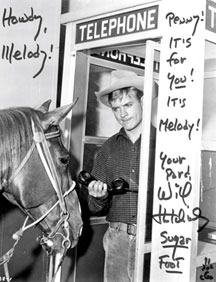 Will Hutchins in phone booth holds phone out to horse Penny.