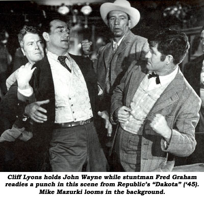 Cliff Lyons holds John Wayne while stuntman Fred Graham readies a punch in this scene from Republic's "Dakota" ('45). Mike Mazurki looms in the background.