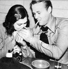 Wayne Morris lights a cigarette for Priscilla Lane during “Virginia City” premiere festivities.