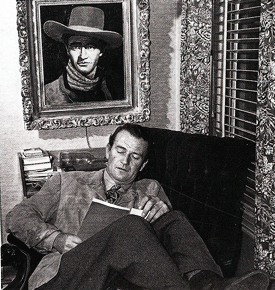 John Wayne looks over a script in his home den. Portrait on the wall is by 
artist John Decker. 