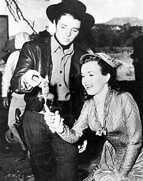 aking a break from filming “The Kid From Texas”, Audie Murphy holds up a bird? in order to let Gale Storm admire it. 