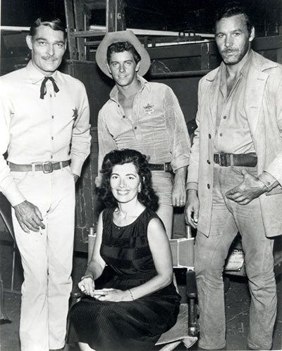 Taking a break between scenes of Warner Bros.’ “Lawman” are John Russell, Peter Brown, badman Chris Alcaide and his wife Peri Alcaide, a noted foreign corespondent. Note the cigarette in Russell’s hand.