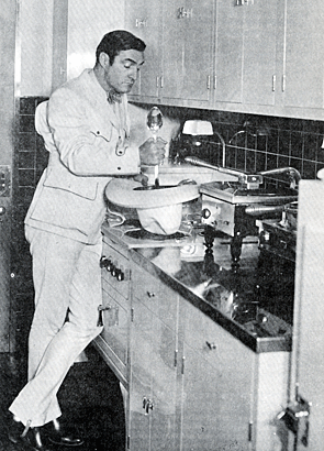 Tom Mix at home in his fully modern electric kitchen prepares some special Western brew...IN HIS HAT??? 