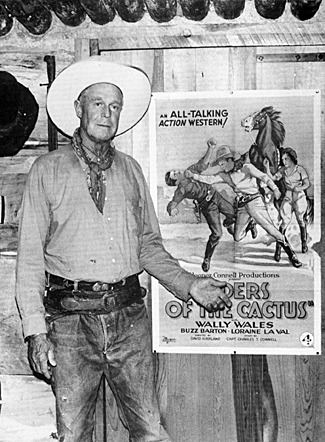 Wally Wales stands beside a poster of his 1931 Big 4 B-Western, “Riders of the Cactus”. 