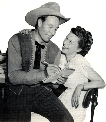 1947 publicity shot of Bill Elliott in a role reversal pose as he jots down dictation from his business manager Sally Thro.