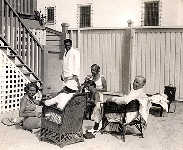 Hoot Gibson and family relax on the beach. That's a waiter with a tray 
in his left hand.