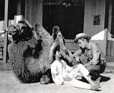 Child actor Ricky Vera snuggles up to a camel and talks with “Broken Arrow” series star John Lupton between scenes of the December 1956 episode “Cry Wolf”.