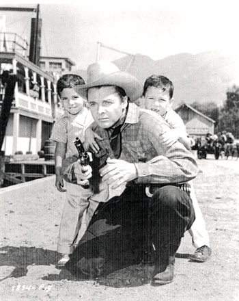 Terry, 6, and James Shannon, 4, seek protection behind their father Audie Murphy in this posed photo on the set of “Ride a Crooked Trail” (‘58 Universal).