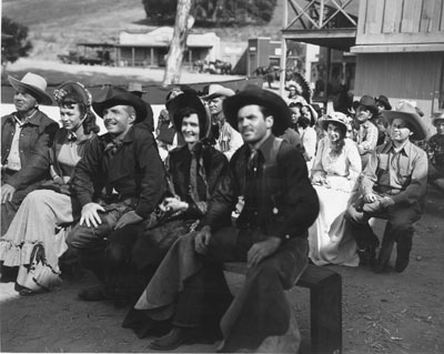 Photo taken during the making of “Lawless Rider” (‘54 U.A.) with Johnny Carpenter (third from left). Stuntman/actor Lou Roberson is on the right. Roberson was stuntman Chuck Roberson’s brother. Known in the business as a ‘high man’, he was killed in a bar fight in the ‘70s. Producer Alex Gordon, who also was an extra in the film, is behind Roberson in the large hat. (Thanx to Tom Weaver.)