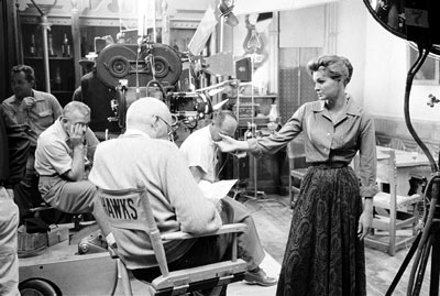 Angie Dickinson discusses her “Rio Bravo” script with director Howard Hawks. Note in the first photo John Wayne is mostly obscured by the camera, but by the second photo he has walked into the background.