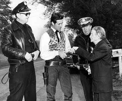 When neighbors became alarmed over the above gunfire, police were called. Here officers Melbie and Henkin observe as Al Jennings shows Hugh O’Brian how Colts were handled in the old days.