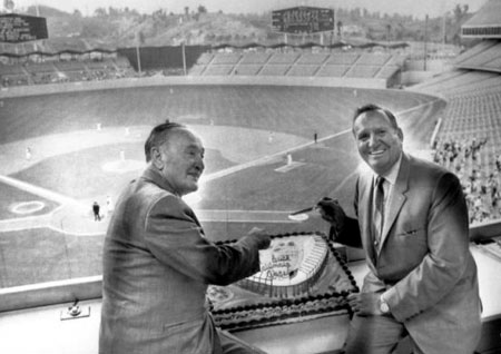 Angels General Manager Fred Haney and Chairman of the Board Gene Autry celebrate the last game the team played in Dodger Stadium as a home team by cutting a cake in the press box during a double header. The cake is decorated with a replica of the Angels’ new stadium in Anaheim.