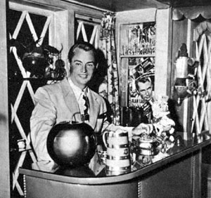 Alan Ladd stands behind his home bar decorated with posters from his films. Photo taken in late 1944.