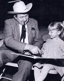 Tex Ritter helps young Heather Moore read her storybook backstage while waiting to go on for a show at the Denver Red Rocks Amphitheater.