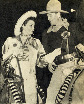Rodeo Queen Jane Russell and Grand Marshal John Wayne compare their official badges as they wait for the Grand Entry Parade which they led.