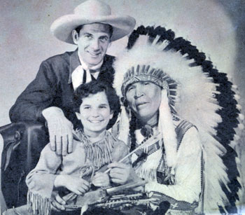 Radio Red Ryder Reed Hadley smiles as his Little Beaver, Tommy Cook, is “adopted” by Chief Thunder Cloud circa 1942.