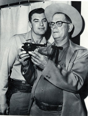 John Bromfield, TV’s “Sheriff of Cochise”, shows his pistol to Jack Howard, the real Sheriff of Cochise County, while they were waiting for the 1957 Tucson Rodeo Parade to begin.