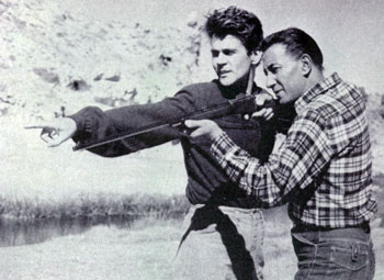 Actor Don Murray and Hollywood’s leading technical expert on weapons, Rodd Redwing, work on a scene for “From Hell to Texas” (‘58). In the movie Rodd fired live ammo from a .30 caliber M1 into a watering trough behind which Murray was hiding. Midway through the trough Rodd had placed a steel plate to stop the bullets. The holes and spurs of water that resulted made the scene very realistic. Then as Murray ran from behind the trough Rodd expertly followed him with a barrage that kicked up dust just inches from Murray’s heels.