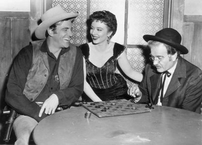 Matt (James Arness) and Doc (Milburn Stone) engage in a friendly game of checkers between “Gunsmoke” scenes as Miss Kitty (Amanda Blake) looks on.