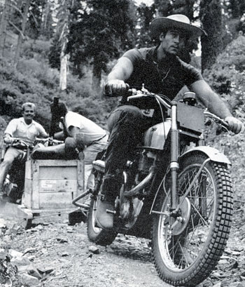 Cint Walker, while panning for gold in the south fork of California’s Feather River, hops on his motorcycle to tow an equipment laden sled by rope. The several hundred pound load included gear, dynamite and aqua lungs.