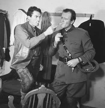 Gregory Peck and John Wayne share a cigarette backstage.