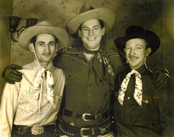 As best we can determine, this photo of Jack Randall was taken in Houston, TX, during a personal appearance in the late '30s. The other two fellows in the photo signed it and put a Houston address in the margin below the photo, possibly hoping Randall could get them into his pictures. Best guess is they are members of a Houston music group as both have on identical bandanas. Fellow on the left signed "Bob Slacy" (or could be Stacy if he forgot to cross his T). Man on the right signed his picture George Christie. Author Merrill McCord who wrote the definitive book on Randall and his brother Bob Livingston, BROTHERS OF THE WEST, tells us he knows Randall sang at his personal appearances, so chances are he used local western musicians to accompany him. (Photo courtesy Gordon Gregersen.)